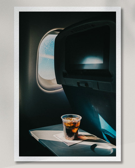 Framed presentation of an aeroplane window, drink and deep blue cabin light