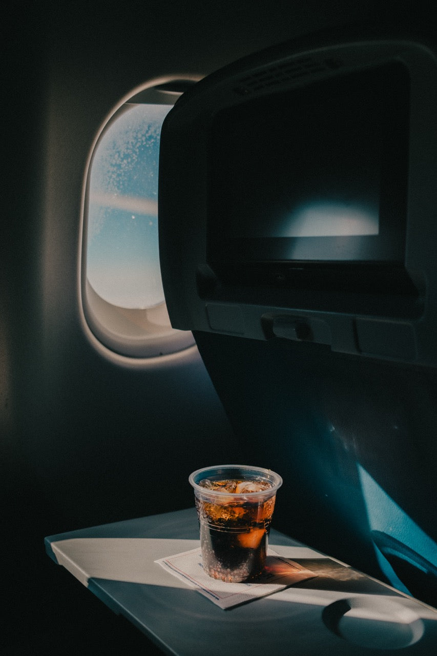 an aeroplane window, drink and deep blue cabin light, photographed by Mitchel Lensink